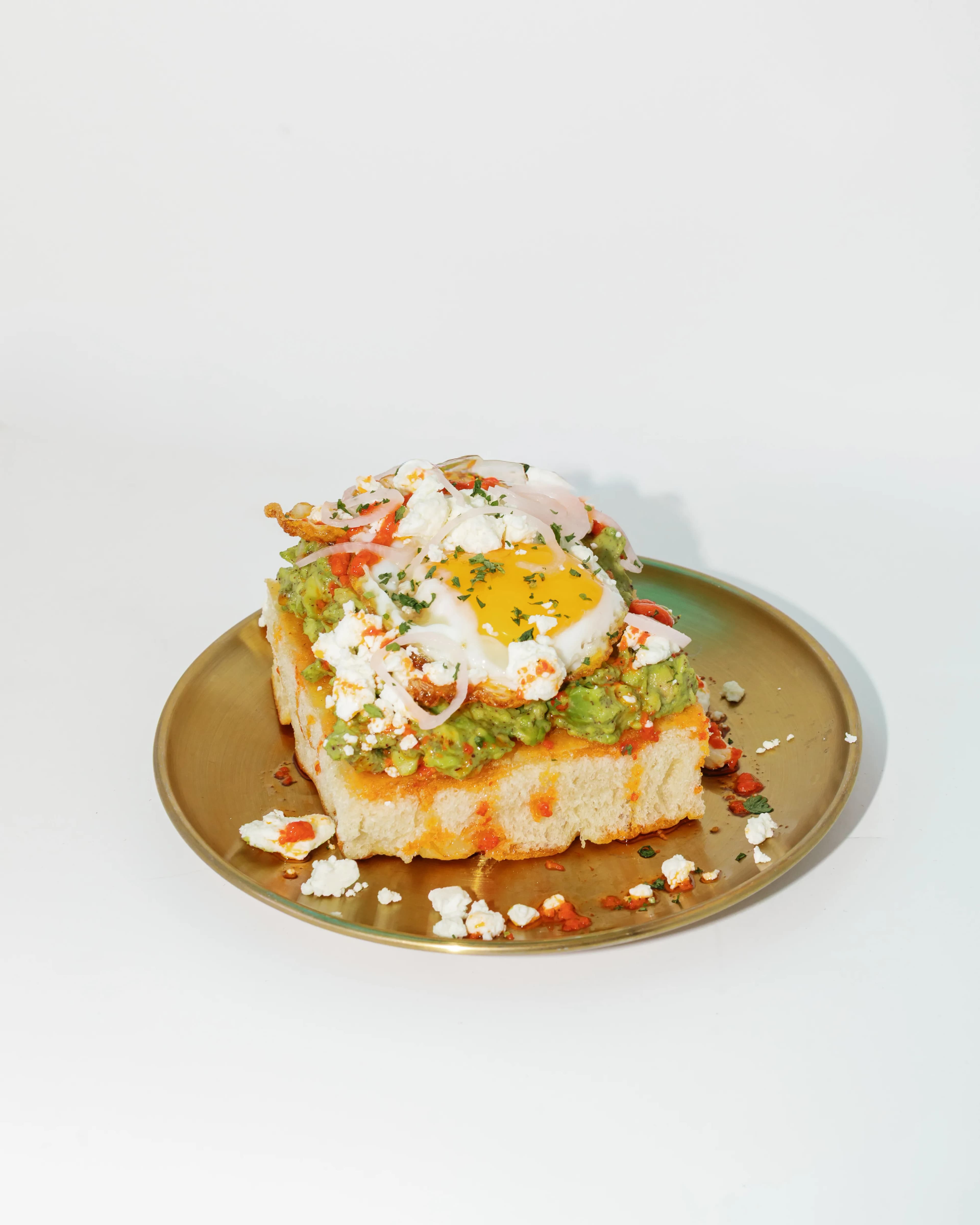 Darling Aviary avocado toast with runny fried egg, crumbled feta and pickled shallots on a gold plate — brunch menu at rooftop bar and restaurant in DoCo, Downtown Sacramento