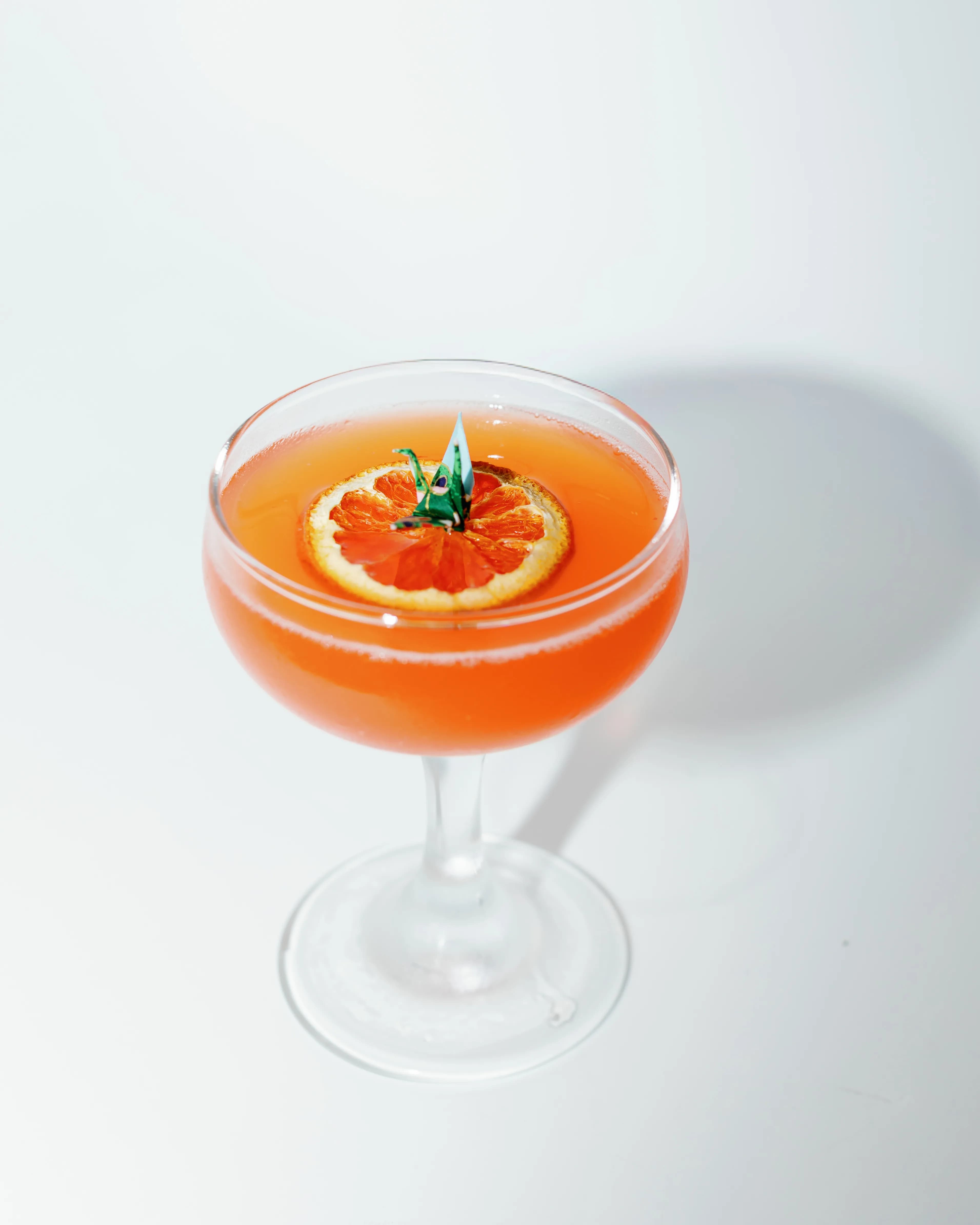 Darling Aviary Paper Plane cocktail in a coupe glass with a dried marigold and fresh orange slice garnish, surrounded by whole oranges and lemons — rooftop bar in Downtown Sacramento